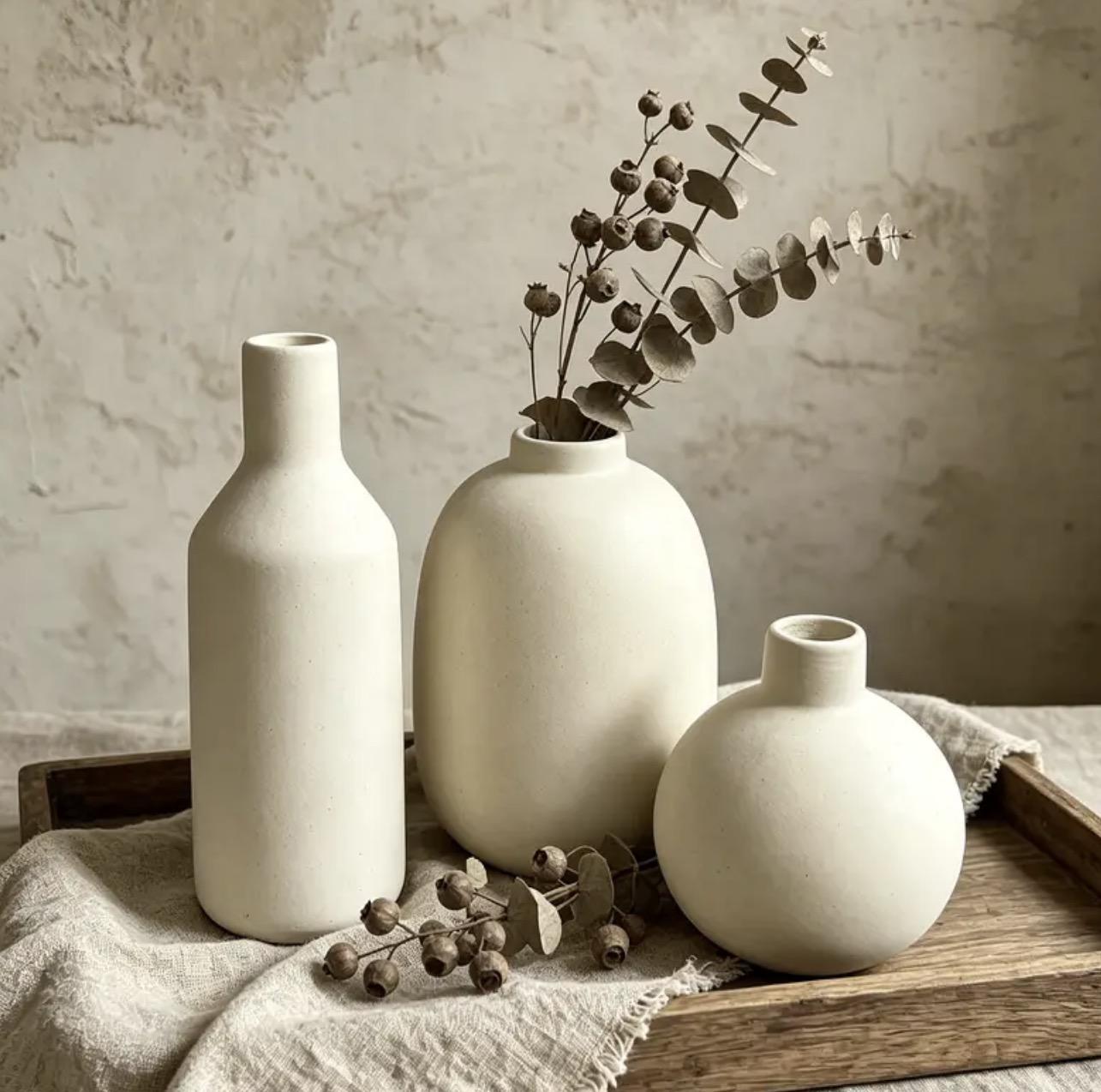 Trio de vases en porcelaine non émaillée sur un plateau en bois avec du lin et des branches d'eucalyptus séché
