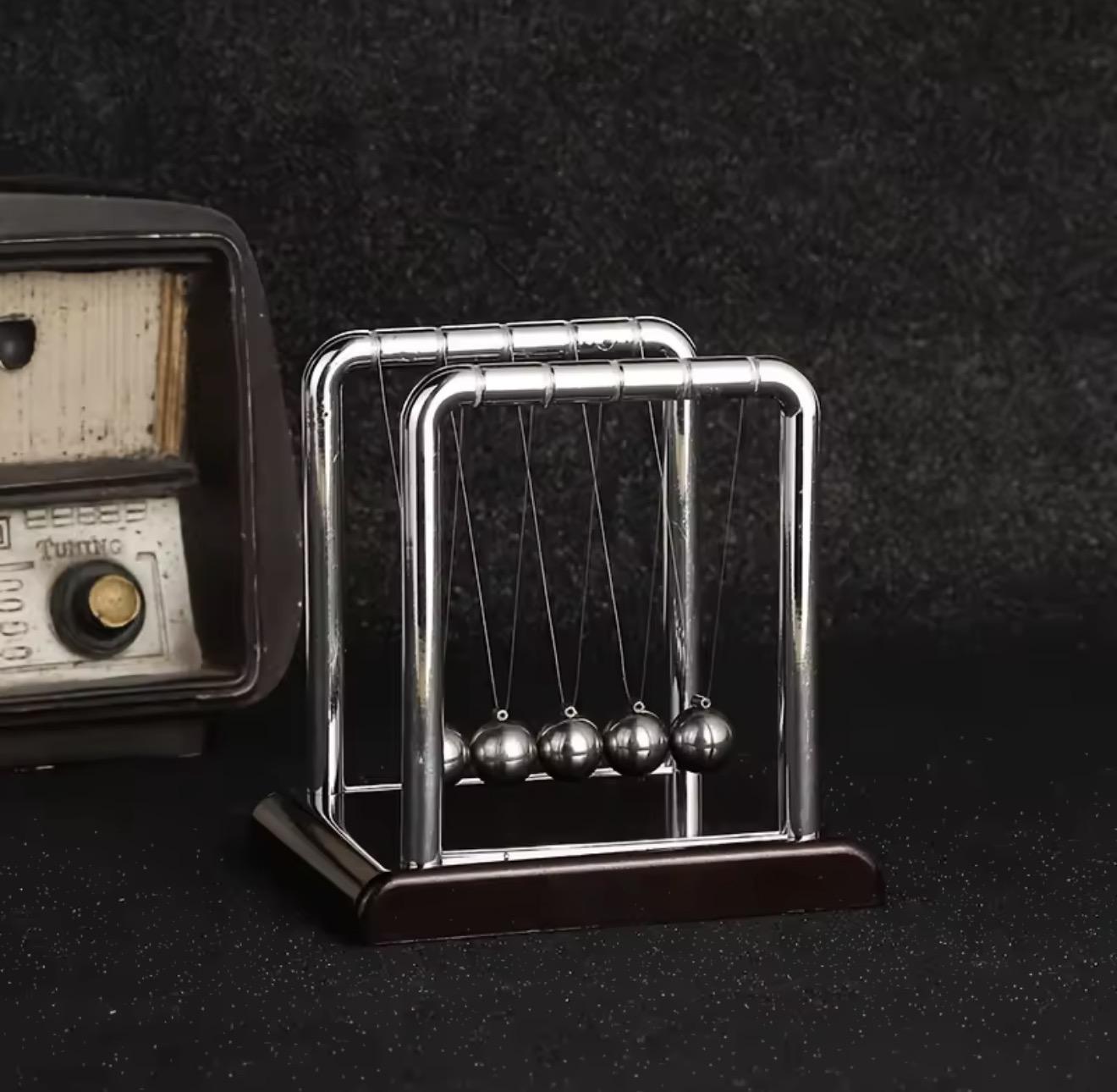 Pendule de Newton en métal chromé à côté d'une radio vintage, fond sombre