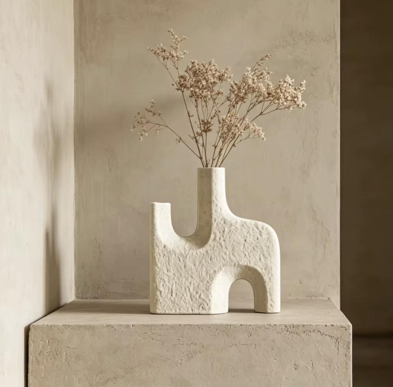 Vase sculptural à texture minérale en forme d'arches, avec des fleurs séchées, posé dans une niche